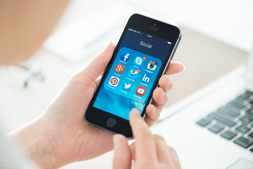 A person is holding a smartphone displaying a folder labeled "Social" with various app icons.