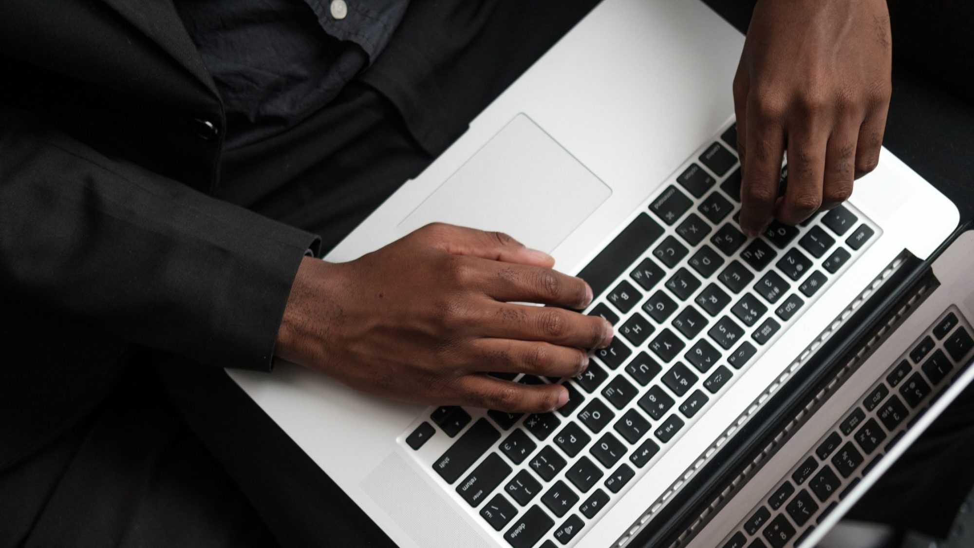 A person wearing a black jacket types on a laptop keyboard, likely reviewing IT policies. 