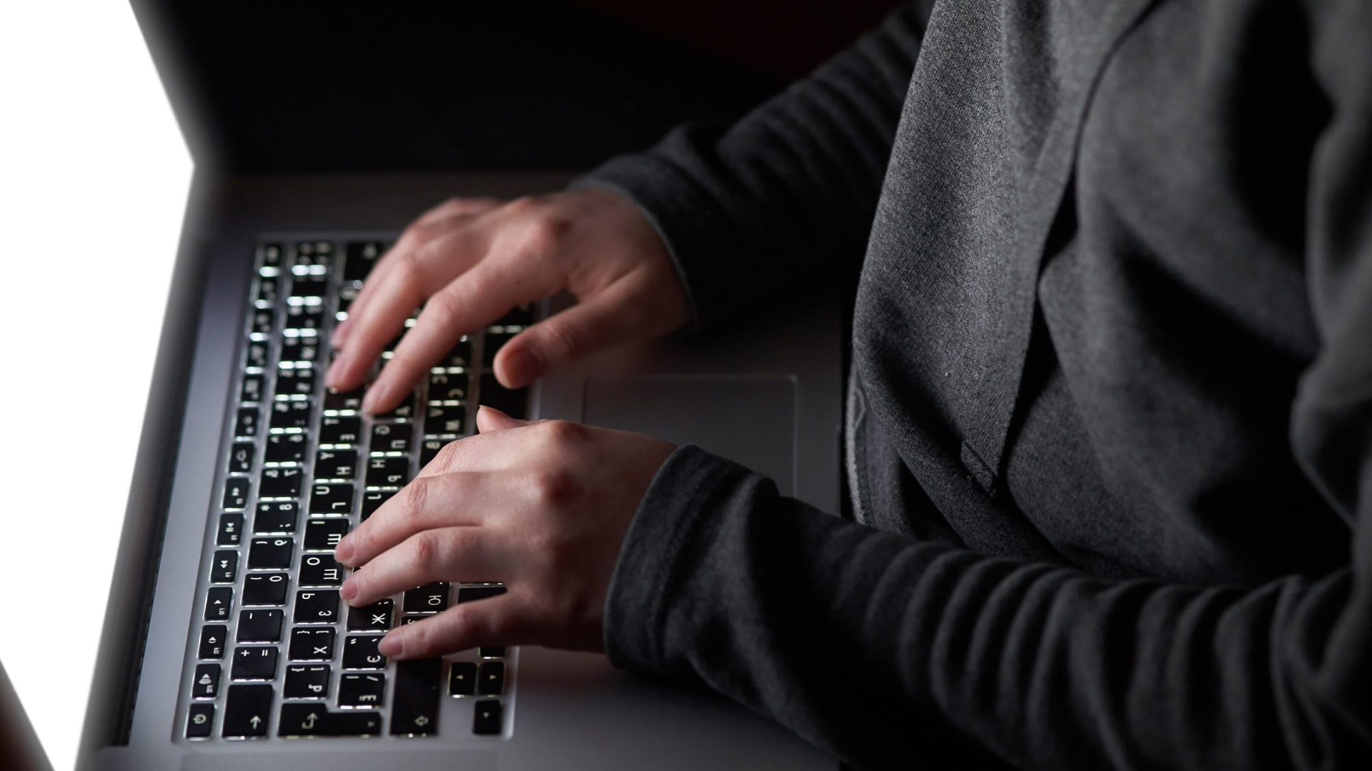Close-up of a person typing on a backlit keyboard of a laptop. 
