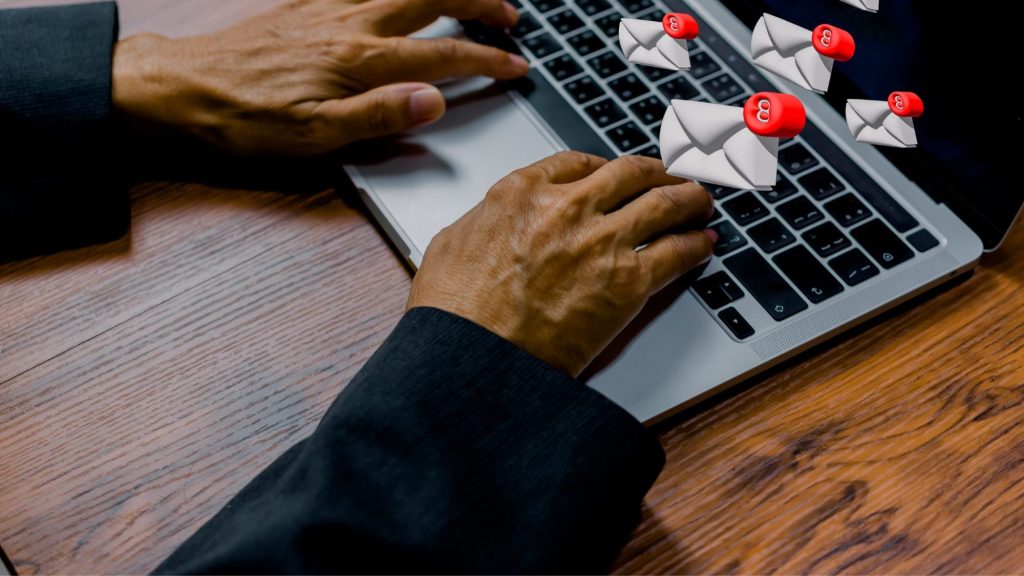 A person is typing on a laptop keyboard with several animated email icons, showing red notification badges, floating above the screen, symbolizing a large volume of incoming emails.