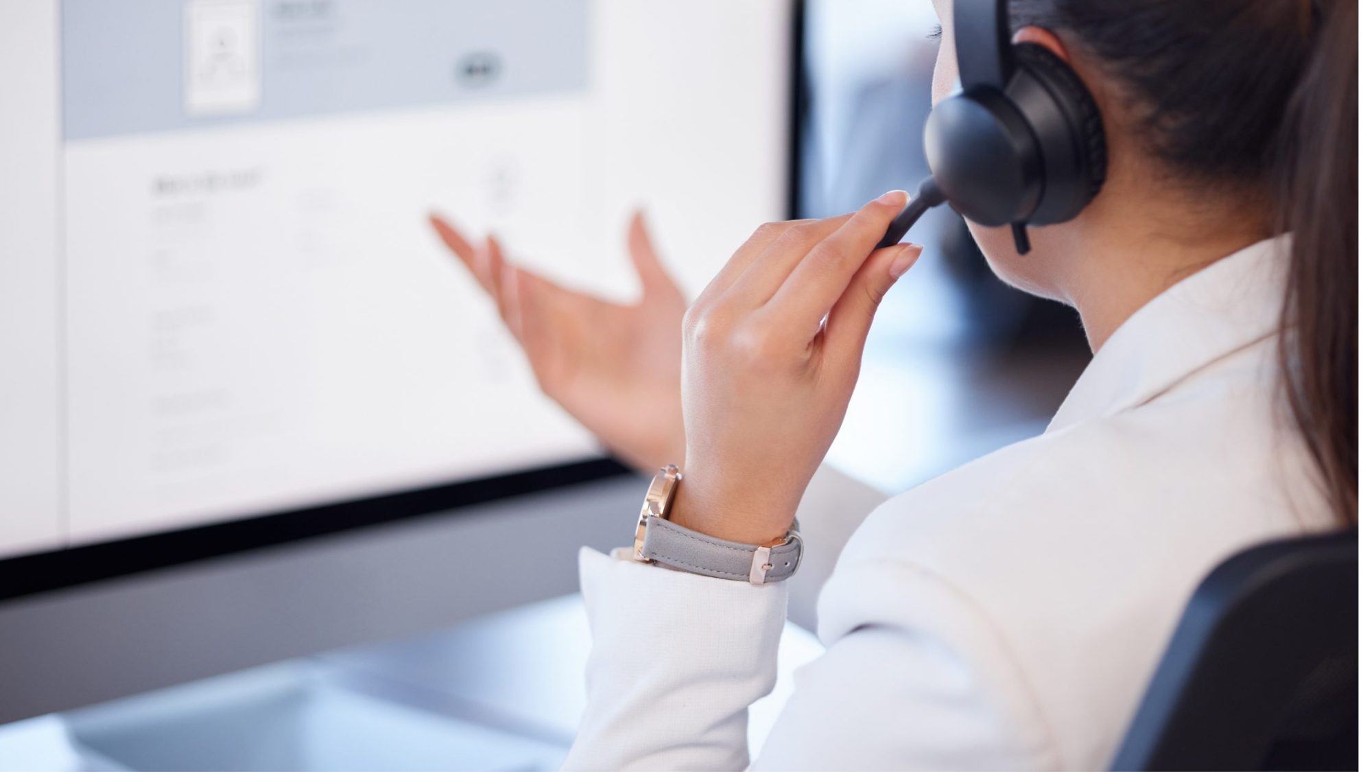 Close-up of a person wearing a headset, gesturing with one hand while looking at a computer screen.
