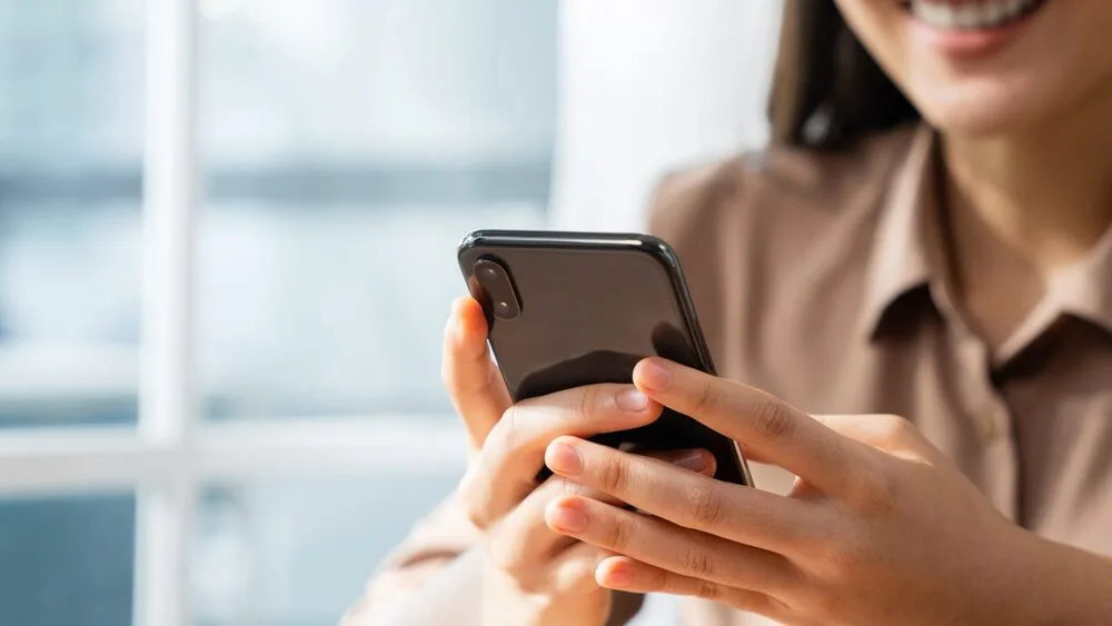 Close-up of a person smiling while holding and using a smartphone.