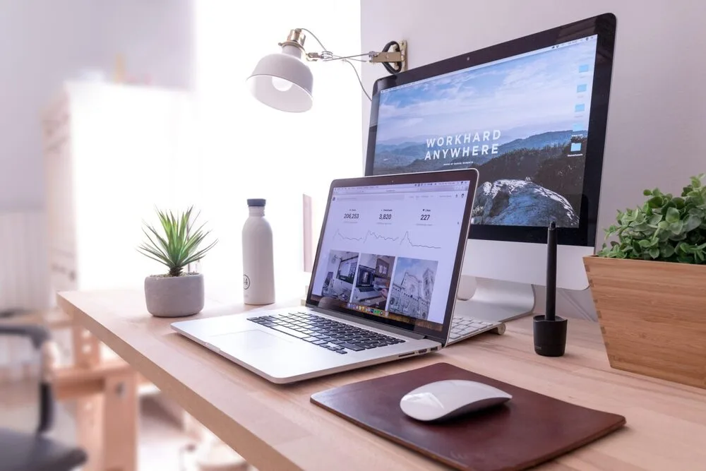 A tidy workspace with a laptop and monitor displaying graphs and a motivational background.