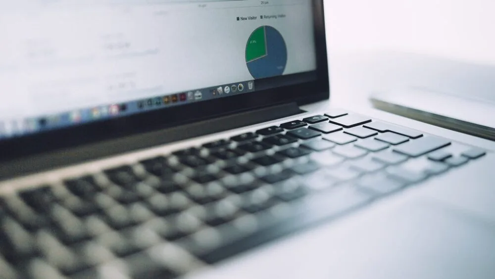 A close-up of a laptop keyboard with an open screen in the background displaying a pie chart and document files.