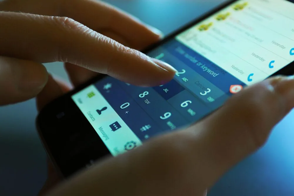 Close-up of a person dialing a phone number on a smartphone touchscreen.