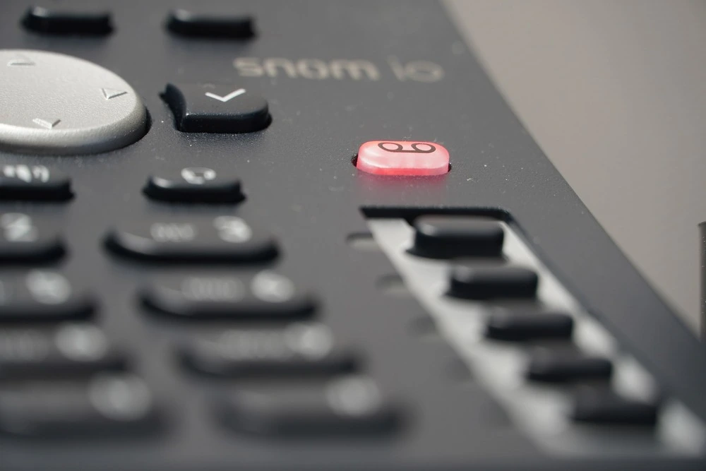 Close-up of a black office phone keypad with a focus on the red voicemail button.