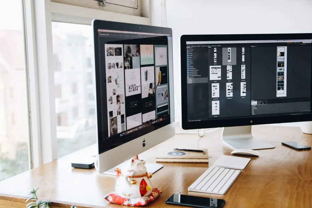 Two computer monitors on a wooden desk display design software.