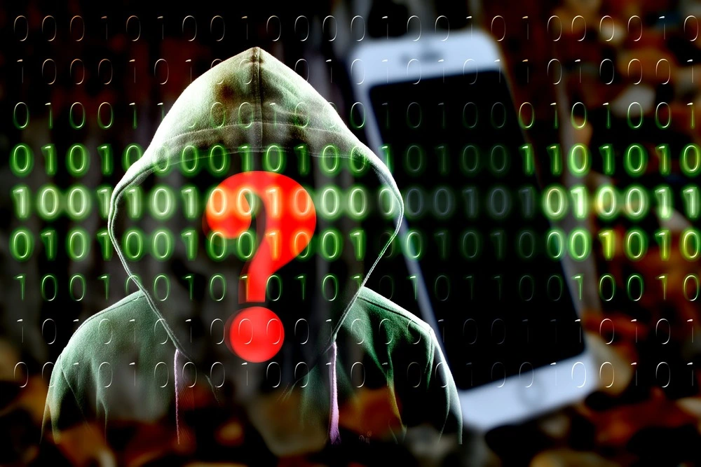 A hooded figure with a red question mark on their face stands in front of a background filled with green binary code.