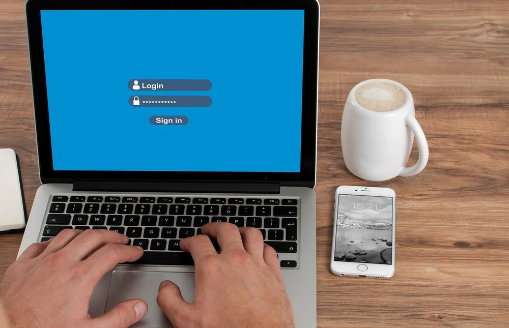 A person typing on a laptop keyboard with a blue login screen displayed.