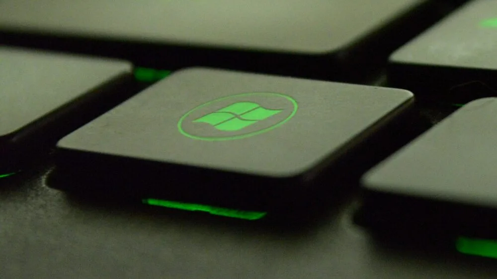 Close-up of a keyboard's Windows key with a glowing green backlight, emphasizing the Windows logo.