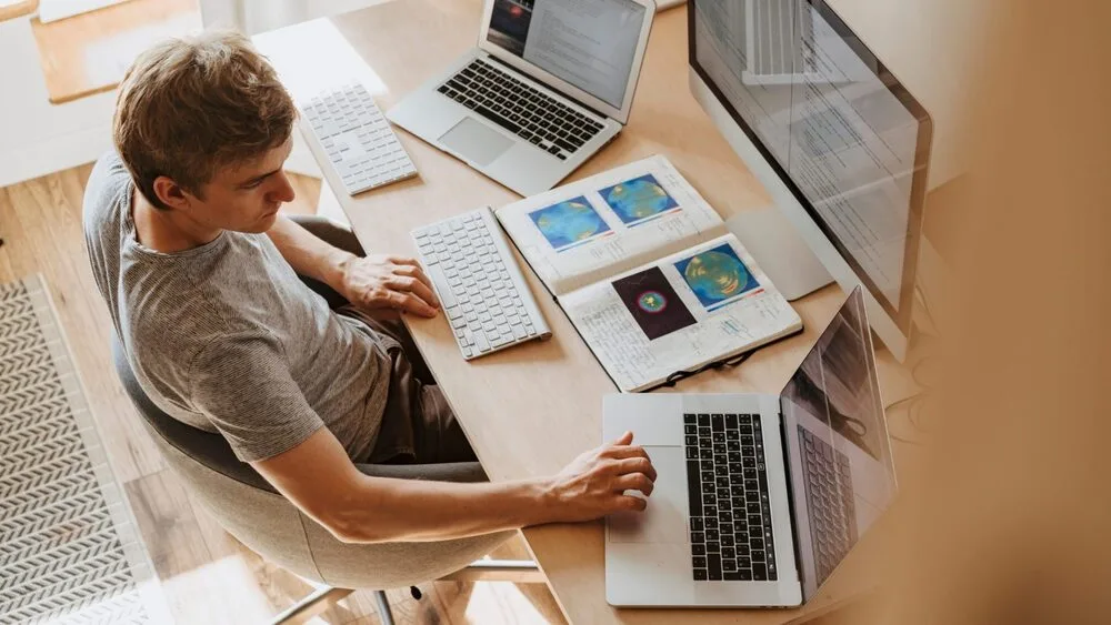 A person sits at a desk using two laptops.