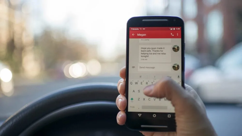 A person is holding a smartphone while driving, with a messaging app open.