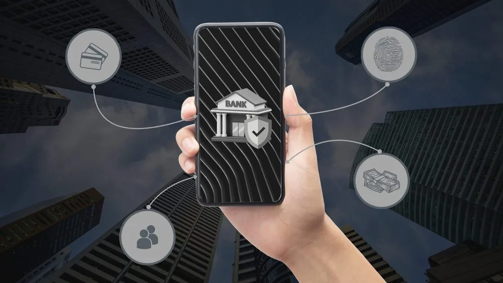 A hand holds a smartphone displaying a bank building icon with a checkmark.