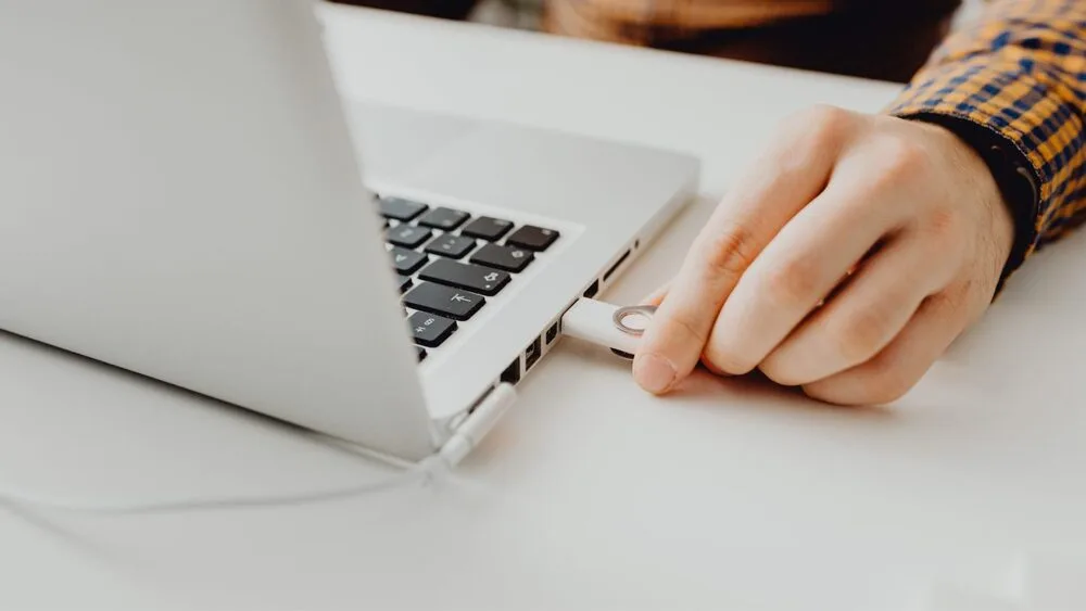 A person is plugging a USB flash drive into a laptop on a white table. 