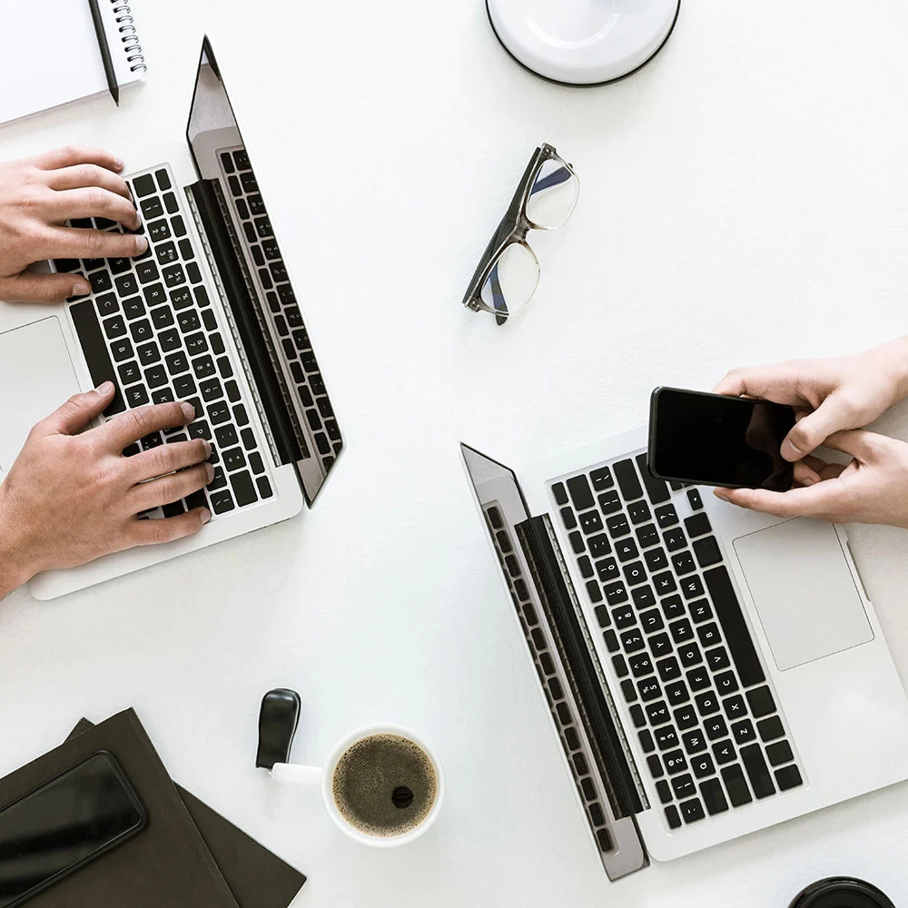 Two people working on laptops at a white table. 