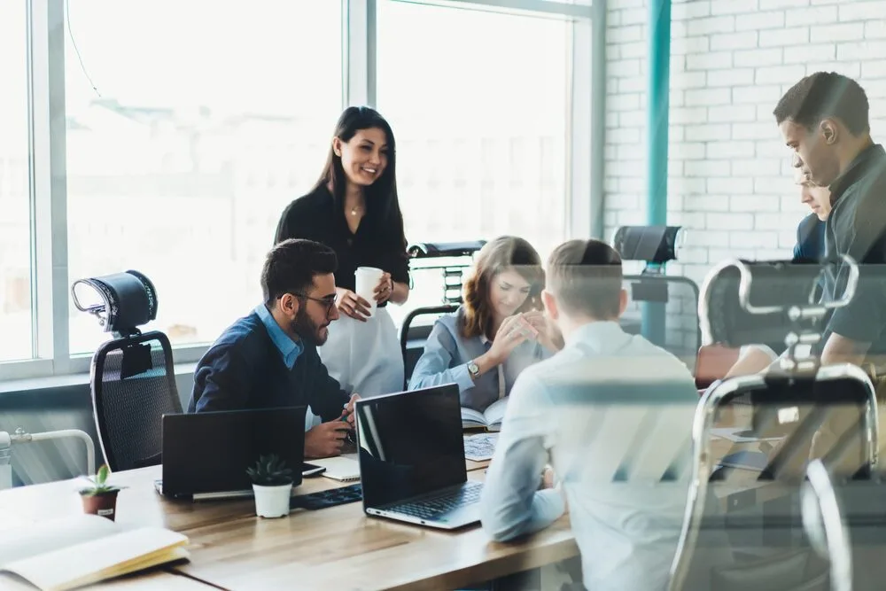 A group of people are gathered around a table in a modern office, working and discussing. 