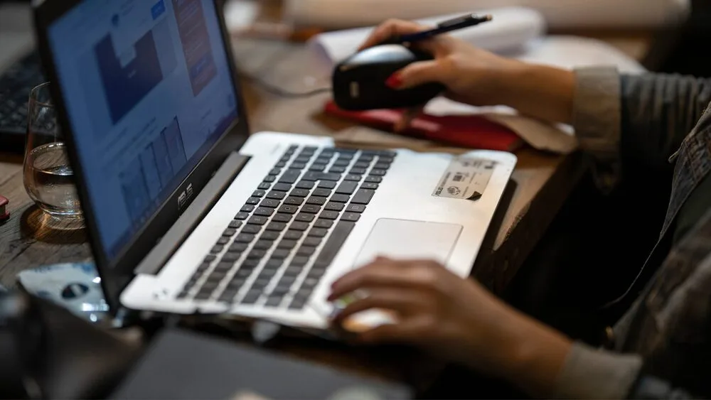 A person is using a laptop, holding a mouse in one hand.