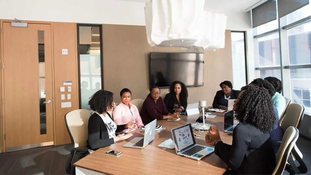 A group of people are sitting around a conference table in a modern meeting room.