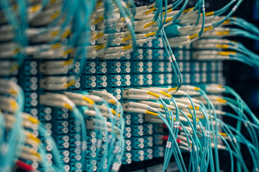 A network server rack filled with numerous teal and yellow fiber optic cables connected to various ports. The image showcases the complexity of data center infrastructure with a close-up, detailed view of the wiring.