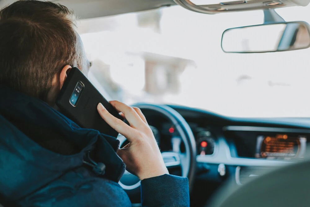 A person is driving a car and talking on a smartphone held to their ear. 