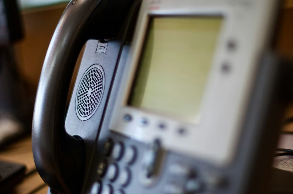 Close-up of an office desk phone showing its keypad and a blurred screen.