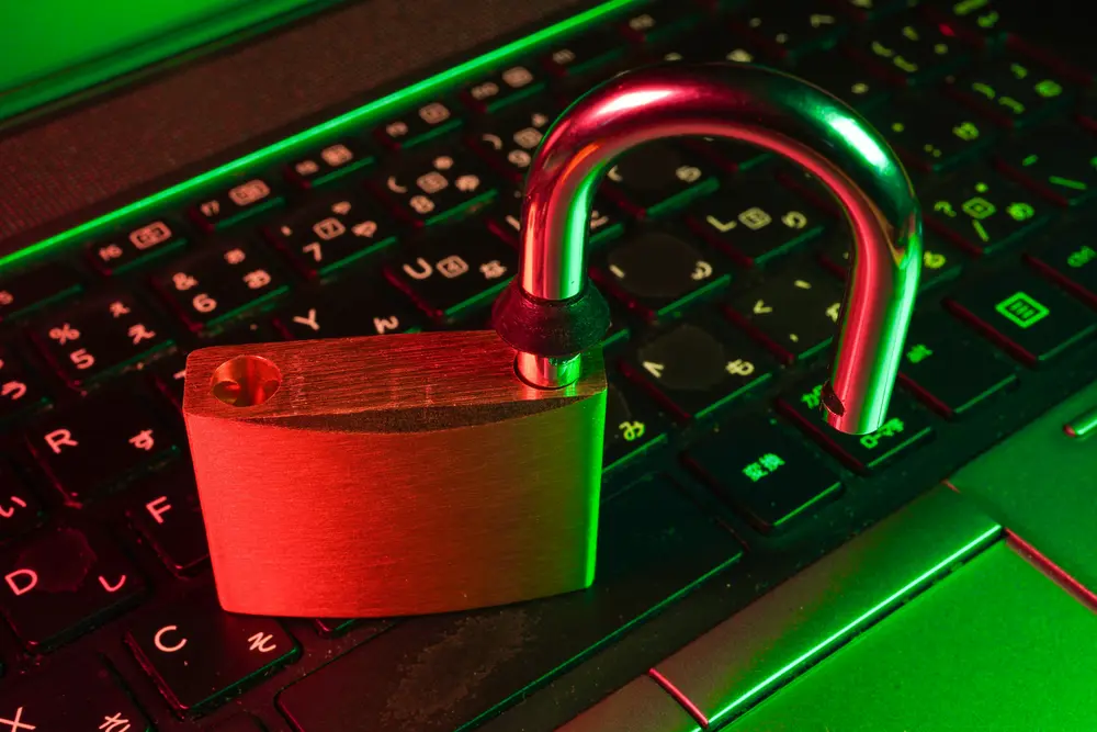 An unlocked padlock rests on a keyboard. The image is bathed in dramatic red and green lighting.