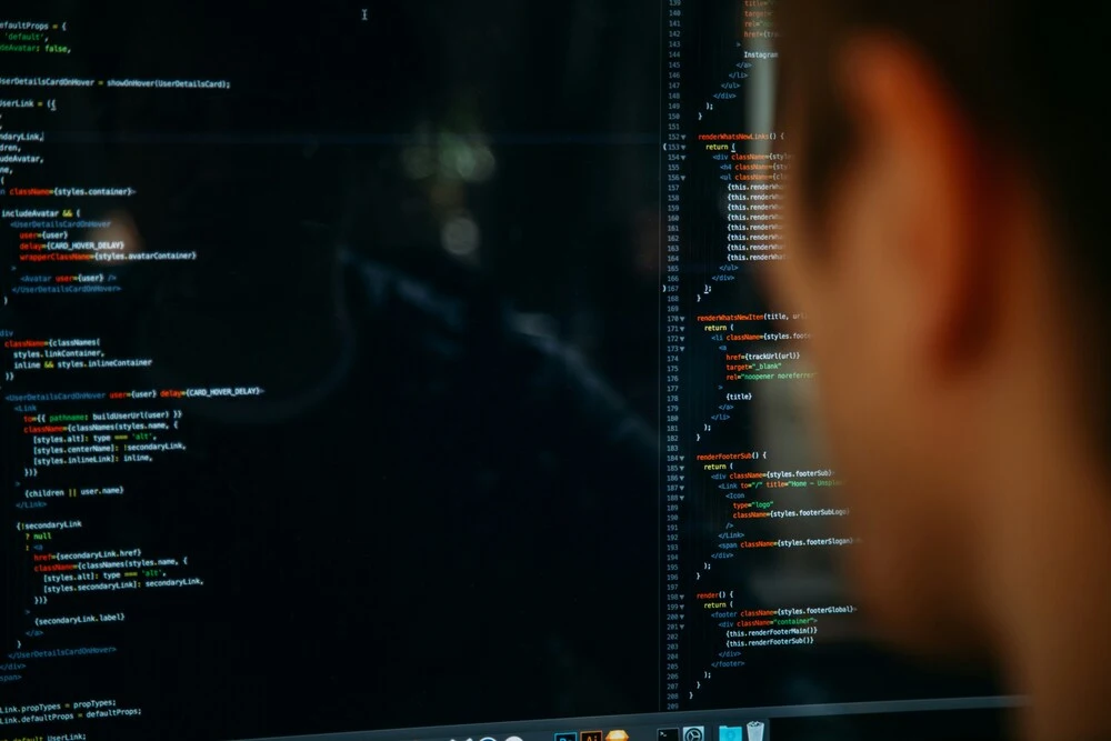 A person looks at a computer screen displaying lines of code in a dark environment. 