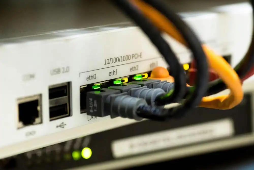 Close-up of a router with multiple Ethernet cables plugged into ports labeled eth0, eth1, and eth2. The ports have green indicator lights, and there are USB ports on the left side of the device.