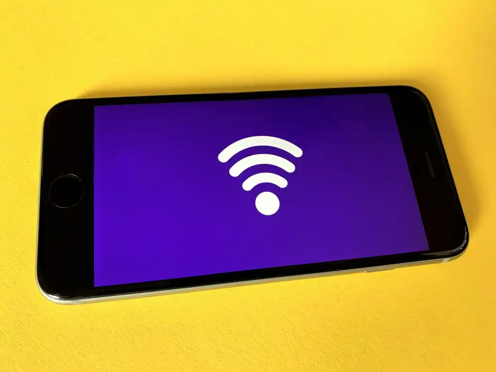 A smartphone lies on a bright yellow surface, displaying a purple screen with a large white Wi-Fi symbol in the center.