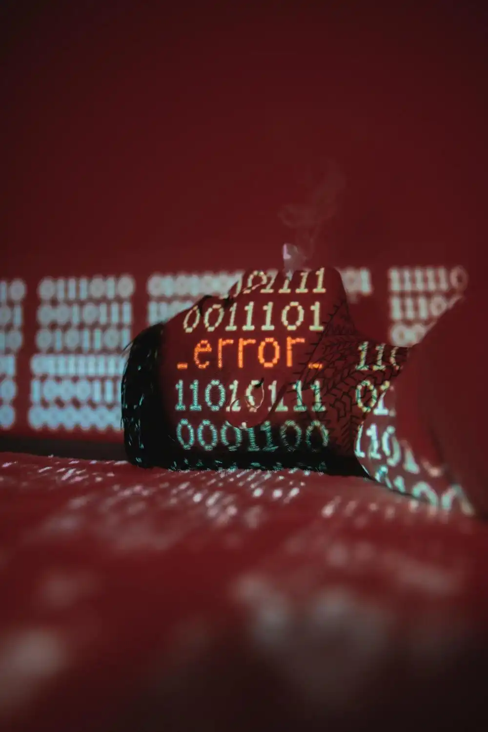 A cracked glass surface with the word "error" displayed in red amid binary code in the background. The scene is illuminated by a red light, creating an intense, digital-themed atmosphere.