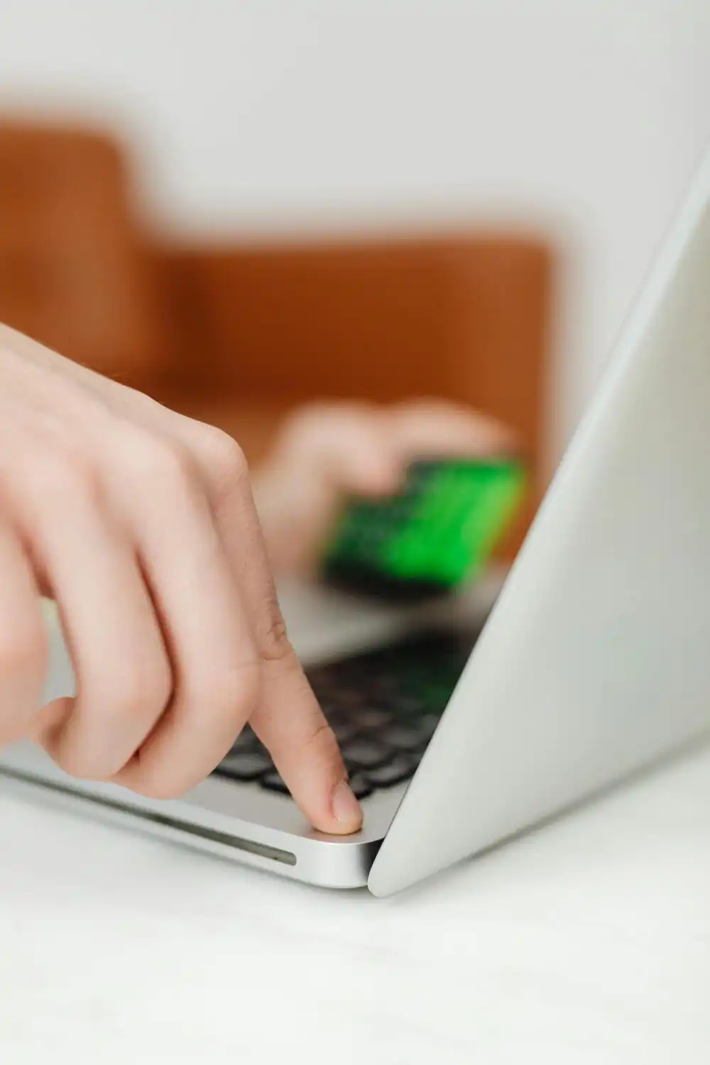 A close-up of a person placing a green credit card near the keyboard of an open laptop, preparing for an online transaction.