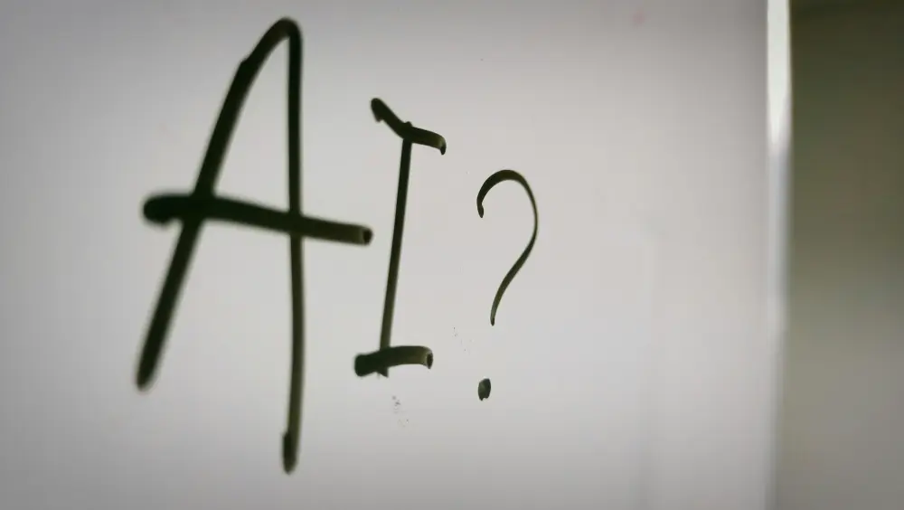 The words "AI?" are written in black marker on a whiteboard, with the letters and question mark large and slightly slanted.