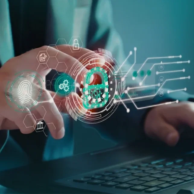 A person's hands interact with a glowing digital interface showing a fingerprint, gears, and a padlock, overlaid on a laptop keyboard, representing cybersecurity and data protection.