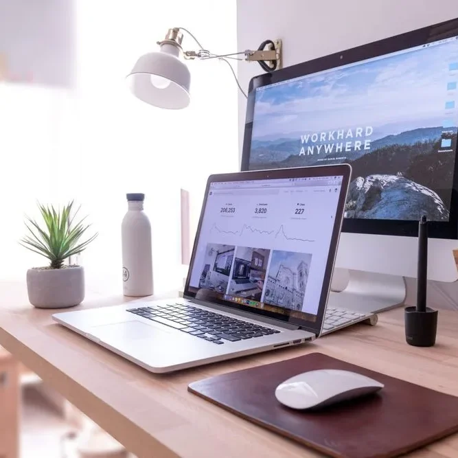 A tidy workspace with a laptop and monitor displaying graphs and a motivational background.