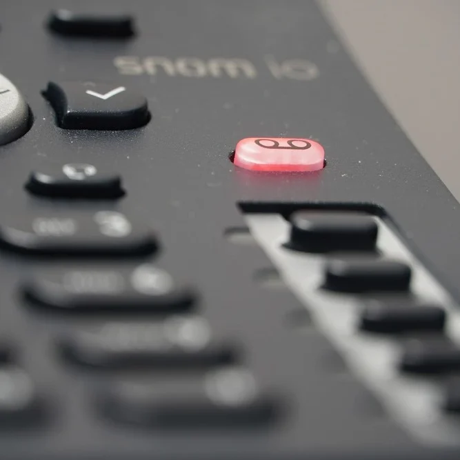 Close-up of a black office phone keypad with a focus on the red voicemail button.