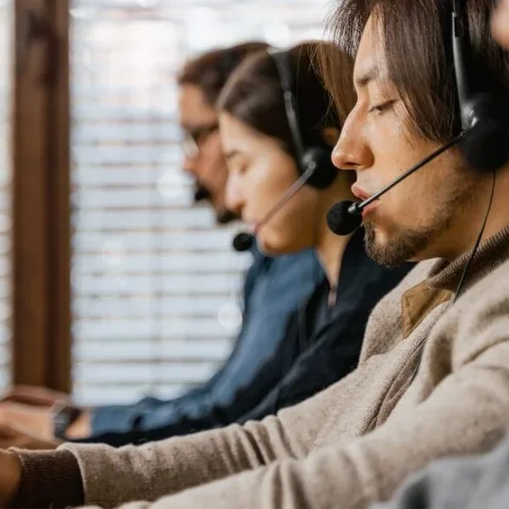 A row of people sitting at desks, each wearing headsets and working on laptops.