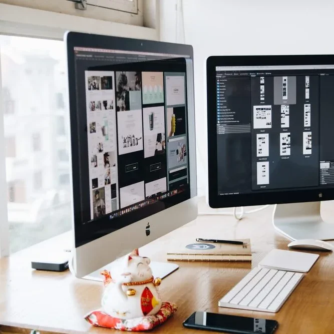 Two computer monitors on a wooden desk display design software.