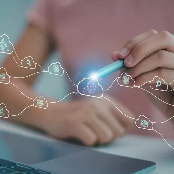 Person using a stylus to interact with a network of cloud icons displayed as holograms above a laptop keyboard.