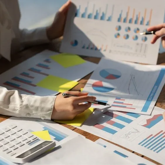 Two people sitting at a wooden table analyzing printed charts and graphs.