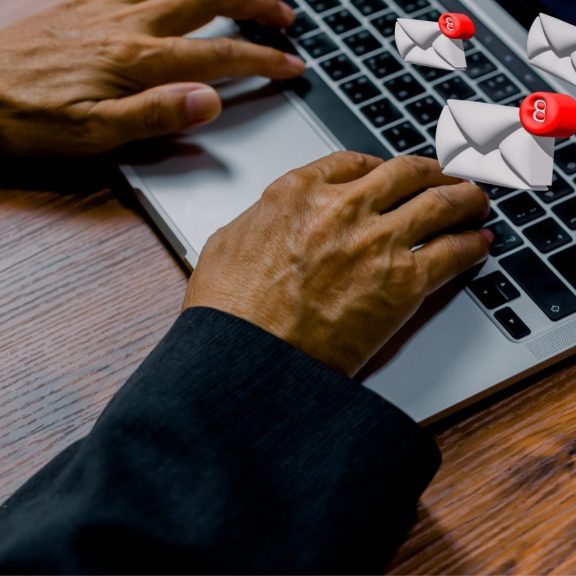 A person is typing on a laptop keyboard with several animated email icons, showing red notification badges, floating above the screen, symbolizing a large volume of incoming emails.