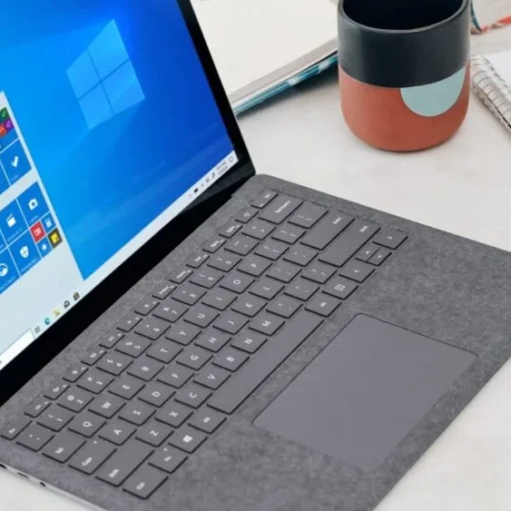 A laptop with a gray keyboard and touchpad is open on a white table displaying the Windows 10 home screen.