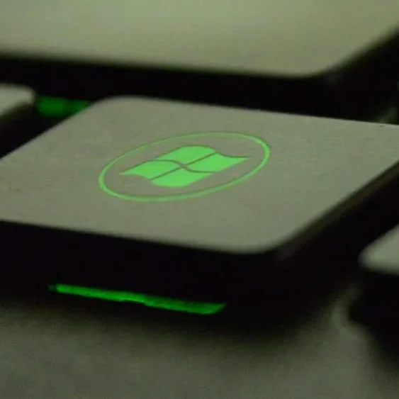 Close-up of a keyboard's Windows key with a glowing green backlight, emphasizing the Windows logo.