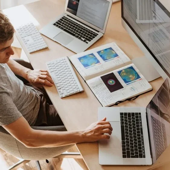 A person sits at a desk using two laptops.