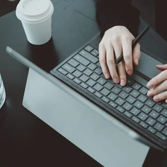 A person is typing on a detachable keyboard connected to a tablet in a dark workspace.