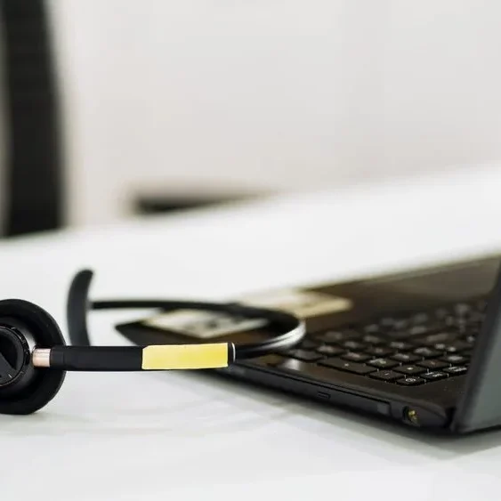 A black headset with a microphone is placed next to a black laptop on a white desk.