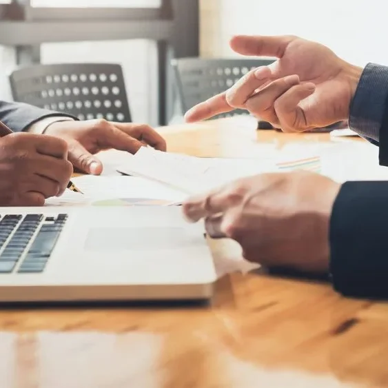 Two people in business attire are sitting at a desk with a laptop in front of them.