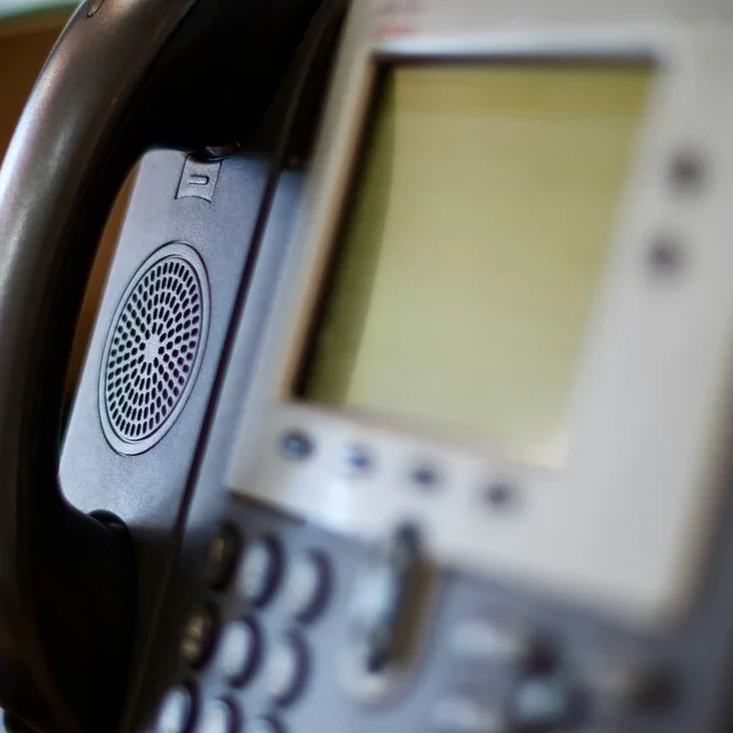 Close-up of an office desk phone showing its keypad and a blurred screen.